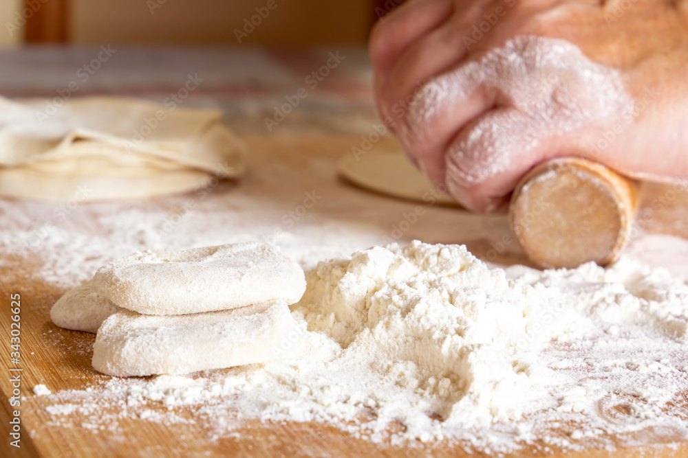 Female hands roll out the dough with a wooden rolling pin on a board with flour. Close-up Female hands roll out the dough with a wooden rolling pin on a board with flour. Close-up