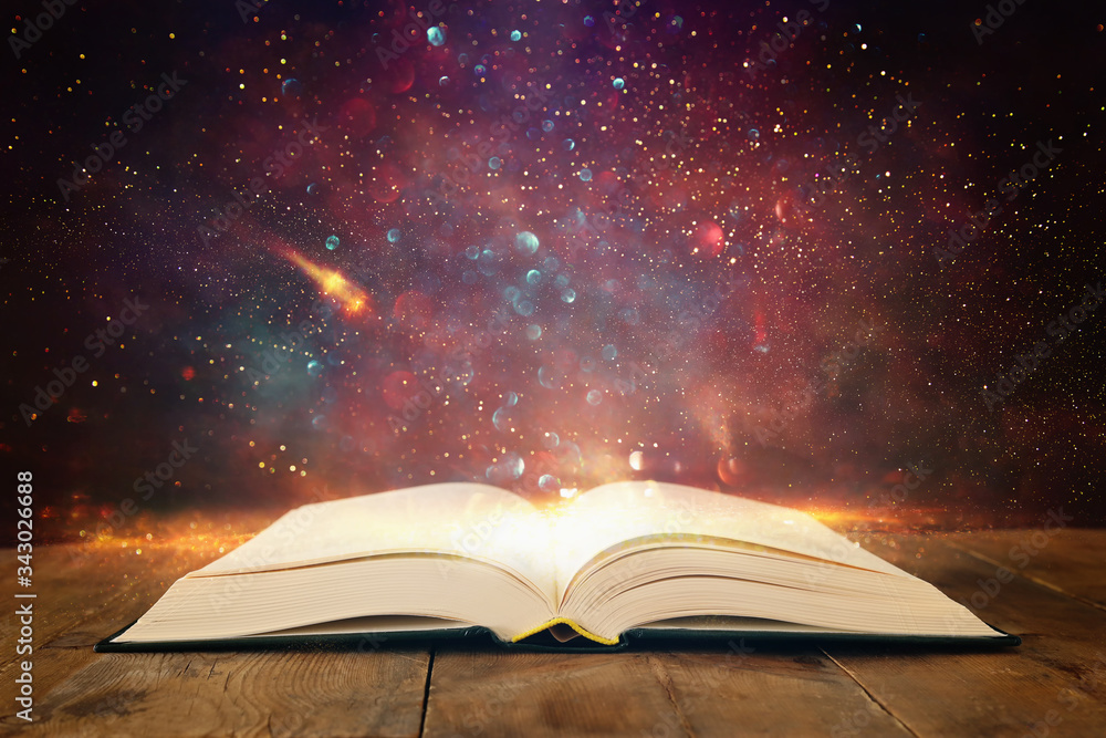 image of open antique book on wooden table with glitter overlay image of open antique book on wooden table with glitter overlay