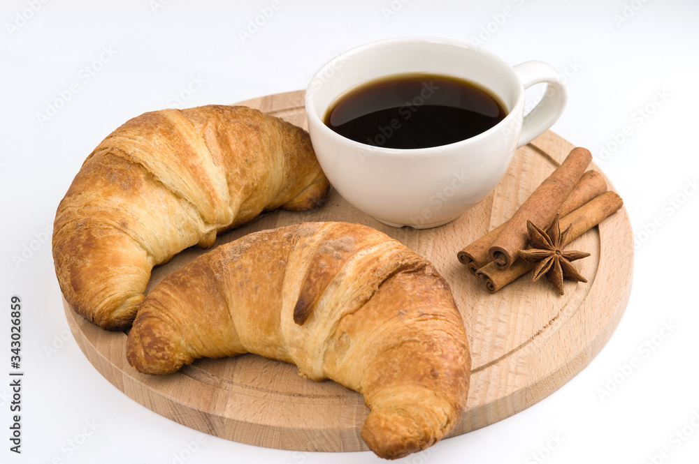 two croissants and a Cup of black coffee with cinnamon are on a wooden Board. White background. two croissants and a Cup of black coffee with cinnamon are on a wooden Board. White background.