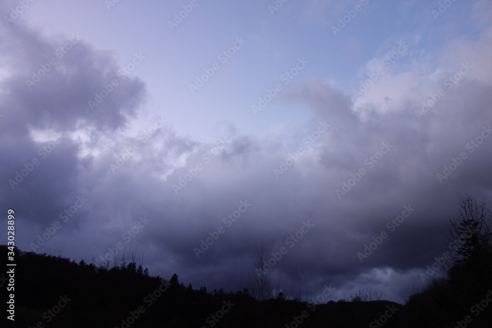 White and grey clouds and grey sky on hills with  trees
