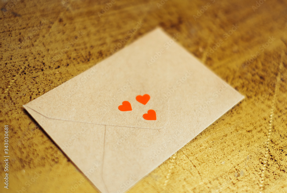 a love letter in a brown envelope decorated with 3 small red hearts on a golden vintage backround