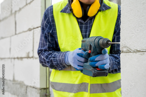 Mechanic uses a drill for drilling walls,Builder worker with a drill machine for drilling aerated bricks at construction site,Construction workers are working using tools.