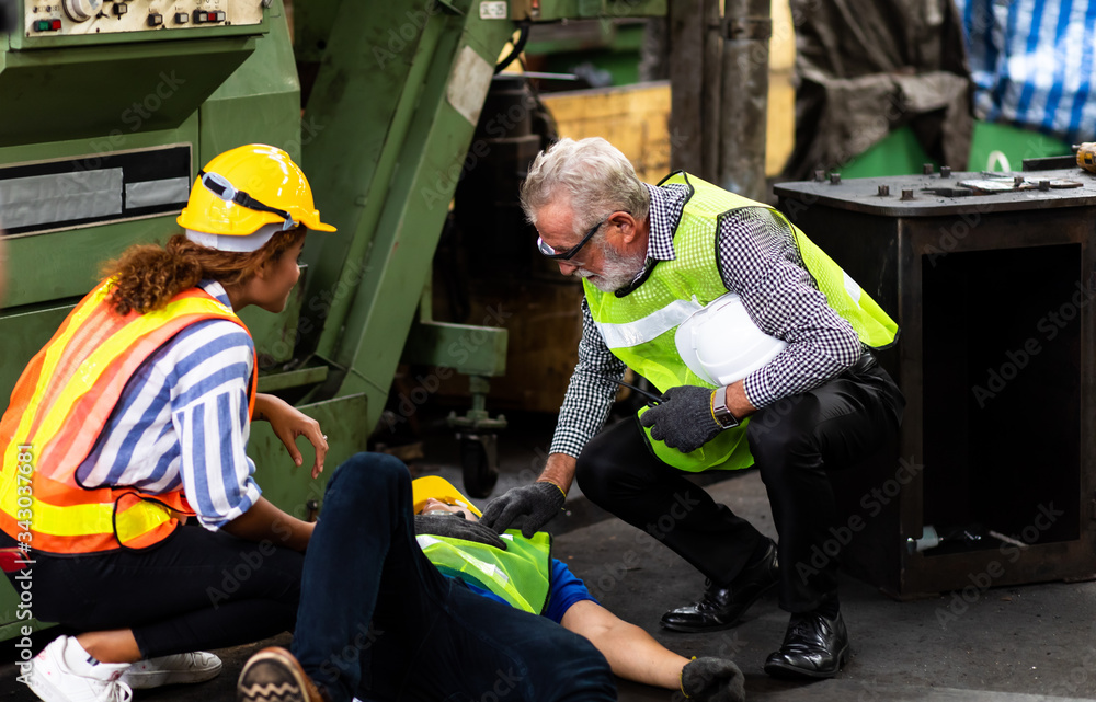 First Aid. Engineering supervisor talking on walkie talkie communication while his coworker lying unconscious at industrial factory. Professional engineering teamwork concept. - obrazy, fototapety, plakaty 