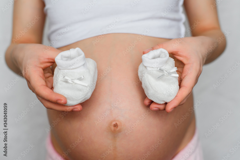 booties for newborn in the hands of a pregnant girl on the background of the abdomen booties for newborn in the hands of a pregnant girl on the background of the abdomen