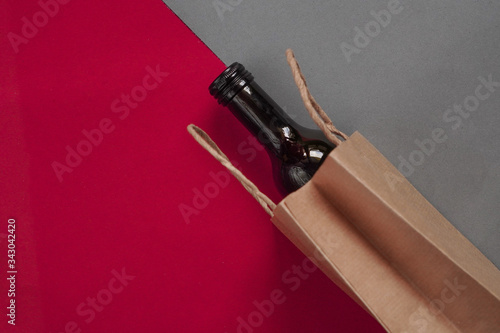 Paper bag with dark glass bottle of wine, alcohol present. Flat lay on maroon background, zero waste. Garbage recycling