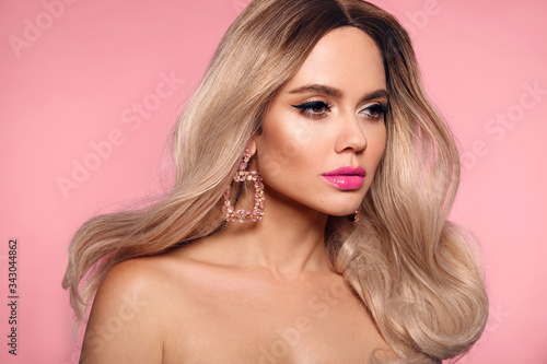 Ombre blond wavy hairstyle. Beauty fashion blonde woman portrait. Beautiful girl model with makeup, long healthy hair style posing isolated on studio pink background.