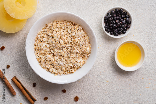 Raw oatmeal with berries, pineapple, honey on a white background. Cooking a healthy breakfast. Top view.