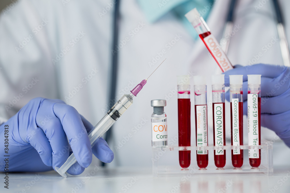 The doctor holding a vaccine to prevent the Covid-19 virus and test tube with blood sample for COVID-19 test, novel coronavirus 2019. The doctor holding a vaccine to prevent the Covid-19 virus and test tube with blood sample for COVID-19 test, novel coronavirus 2019.