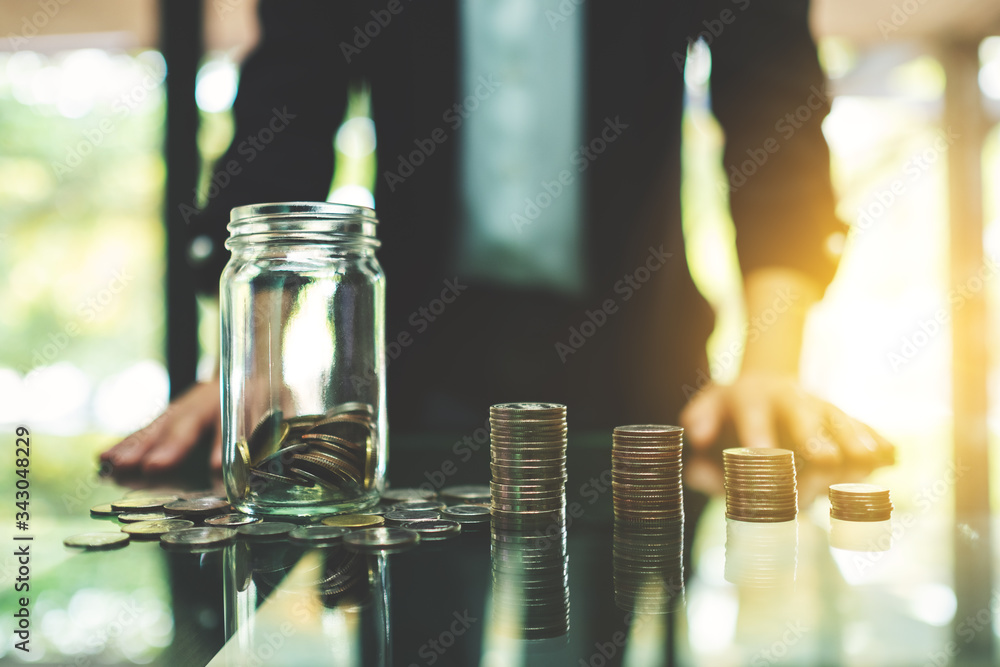 Closeup image of a businessman with coins stack and a glass money jar on the table for saving and financial concept Closeup image of a businessman with coins stack and a glass money jar on the table for saving and financial concept