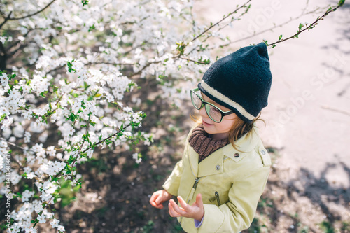 Little girl in big eyeglasses on the background of flowering branches of apple in spring garden