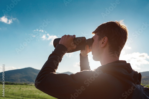 Young man at mountain looking through binoculars