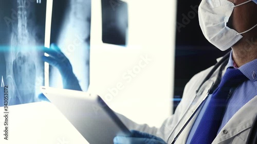 A male doctor in a dark room comparing x-rays displayed on illuminated panels before operation .