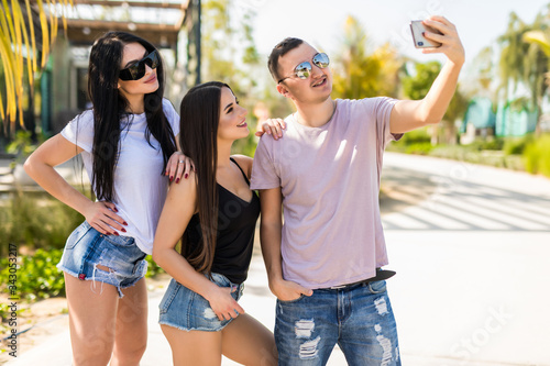 Three young friends, man is taking a self-portrait with two girls are enjoying their summer vacation.