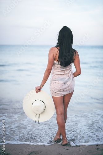 Beautiful dark haired young woman standing on the Mallorca becah holding her nice big hat and watching sea, Enjoying nice view and sunny weather, summer holidays photo