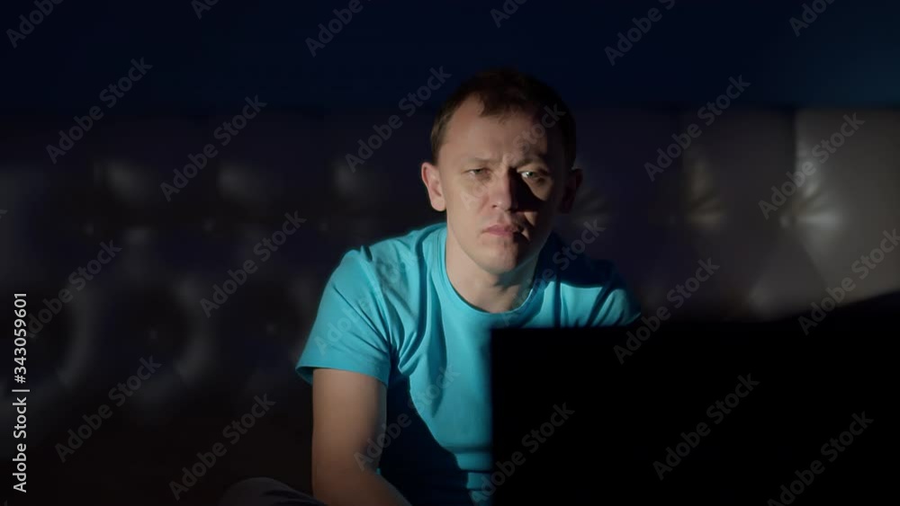 Attractive man sits at home at night on the bed and watches TV, strong emotions Attractive man sits at home at night on the bed and watches TV, strong emotions