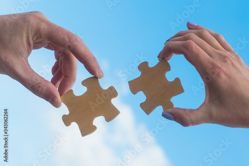 Two hands connect puzzle pieces against the sky. Business concept idea, cooperation, partnership, teamwork, innovation
