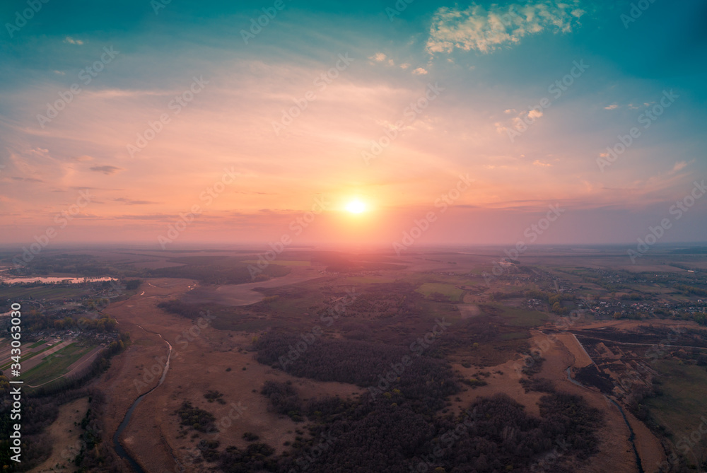 Spring rural landscape in the evening with beautiful burning sky. Aerial view. Panoramic view of pine forest, fields, river, and village during blazing sunset