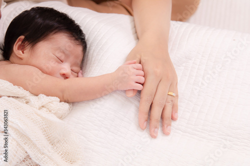 Selective focus touching feeling, tiny fingers newborn baby hold mother hands with wedding gold ring, mom feeding newborn at home, happy infant sleep on bed hold mother finger for protection, safety