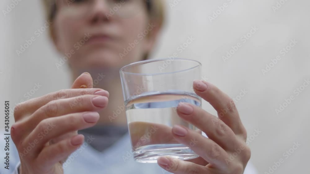 Woman take pills and hold glass of water. Female at home on quarantine. Self isolation. Helthy woman take vitamines Woman take pills and hold glass of water. Female at home on quarantine. Self isolation. Helthy woman take vitamines