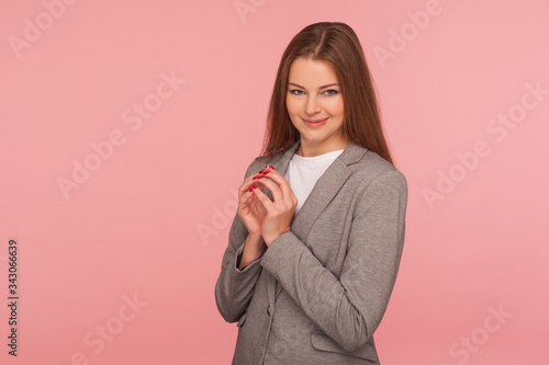 Portrait of beautiful cunning young woman in business suit thinking over devious idea with tricky face expression, scheming and conspiring evil prank. indoor studio shot isolated on pink background