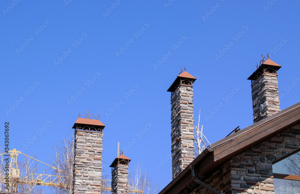 Stone pipes of fireplaces in the house. Element of the facade of house and the roof. Background is blue sky. Construction crane in background. Concept - buying  private home sales, mortgage.