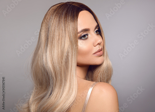 Ombre blond shiny hair. Beauty fashion blonde woman portrait. Beautiful girl model with makeup, long healthy hairstyle posing isolated on studio grey background.