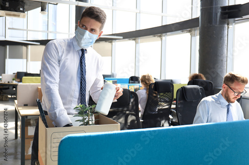 Dismissal employee in preventive medical mask in an epidemic coronavirus. Sad dismissed worker are taking his office supplies with him from office.