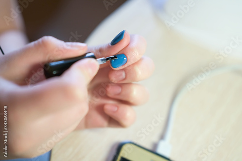 Young woman applying nail polish with brush from bottle  polishing painting fingernails with blue color enamel  doing manicure at home  perfect healthy nails care
