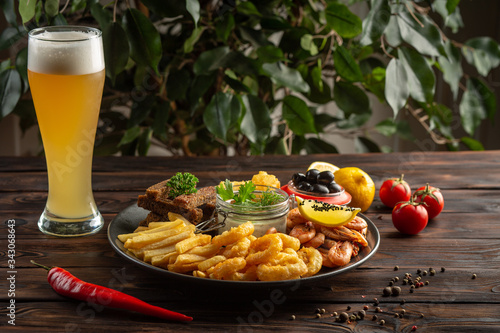 glass of foamy beer and a plate with snacks on a wooden background