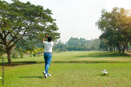 Golf player hitting shot with club on course at beautiful morning with sun flare in background