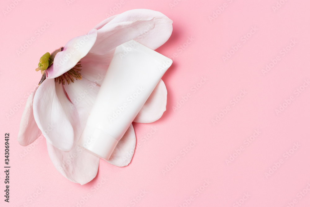 White tube with cream and magnolia flower on pink background, copy space White tube with cream and magnolia flower on pink background, copy space