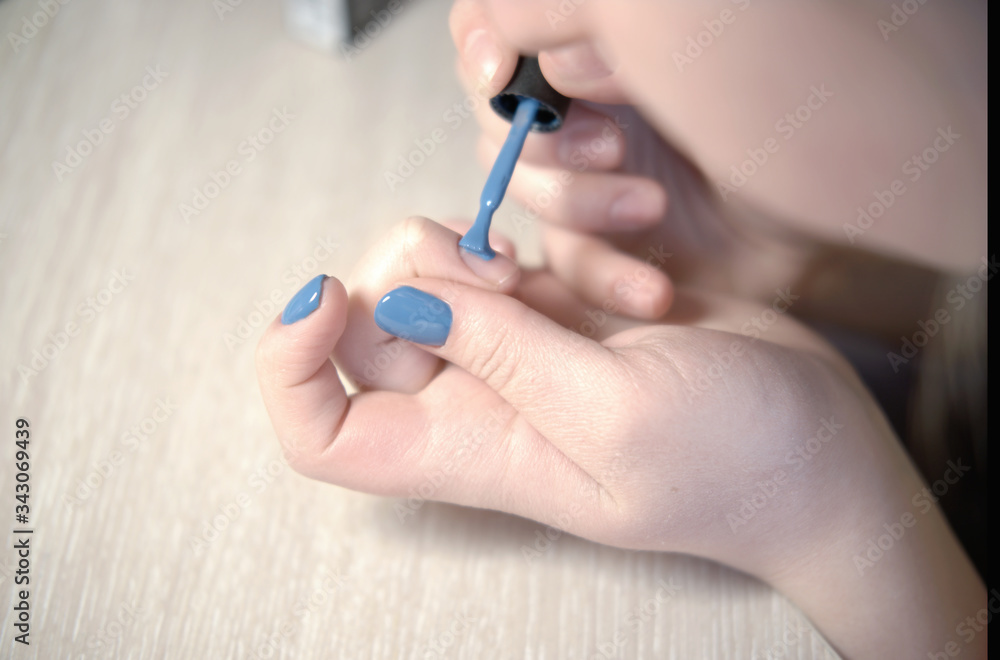 Young woman applying nail polish with brush from bottle, polishing painting fingernails with blue color enamel, doing manicure at home, perfect healthy nails care Young woman applying nail polish with brush from bottle, polishing painting fingernails with blue color enamel, doing manicure at home, perfect healthy nails care