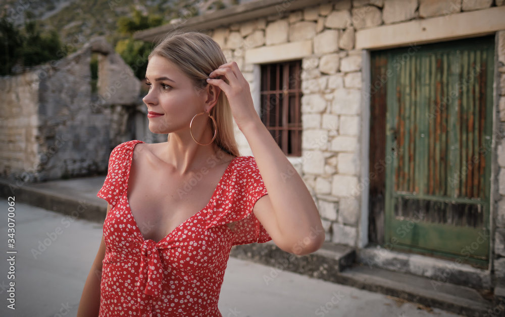 Vogue style elegant portrait of beautiful fashion woman wavy shine blonde long hair. Model in red dress with bright makeup in old town medieval Italy