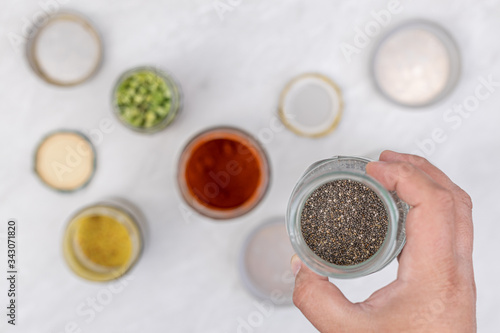 Chia seeds in the jar with jars in the blurred background on the kitchen table. Healthy food concept with chia seeds in the hand