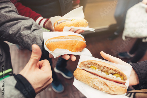 Traditional Dutch sandwiches with herring and pickles in hands. Group of friends trying fish hotdog. Scandinavian cuisine. Selective focus