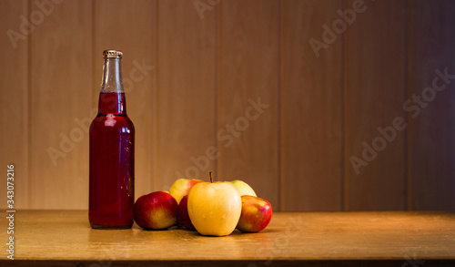 Glass bottle with red apple cider and apples on a wooden background with copy space.