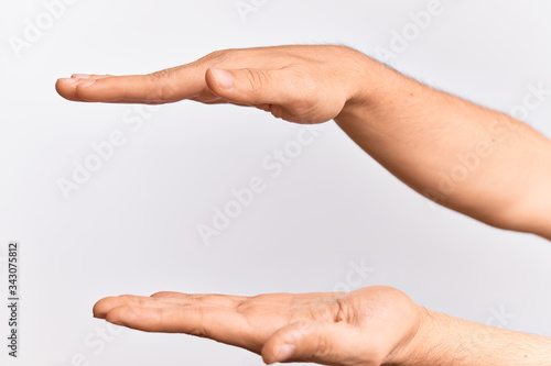 Hand of caucasian young man showing fingers over isolated white background holding copy space between them, measuring with both palms