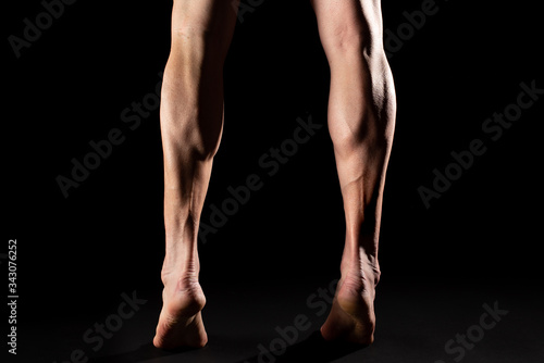 Studio photography of the legs and the calf muscle of a muscular cyclist athlete with black background