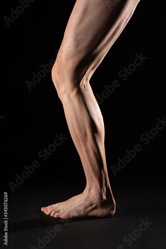 Side view of the leg and calf muscle of a fibrous barefoot cyclist athlete. Studio photography with black background
