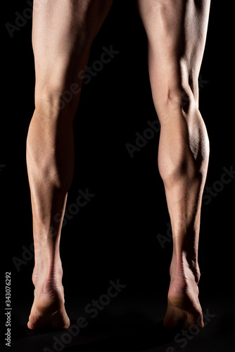 Studio photography of the legs and the calf muscle of a fibrous cyclist athlete with black background
