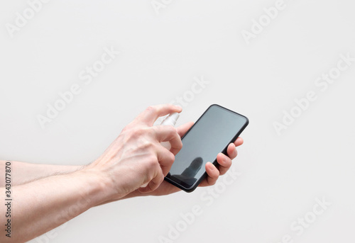 Mobile phone disinfection on a white background. Men's hands cleans the phone with a sanitizer. Prevention of coronavirus, covid-19.