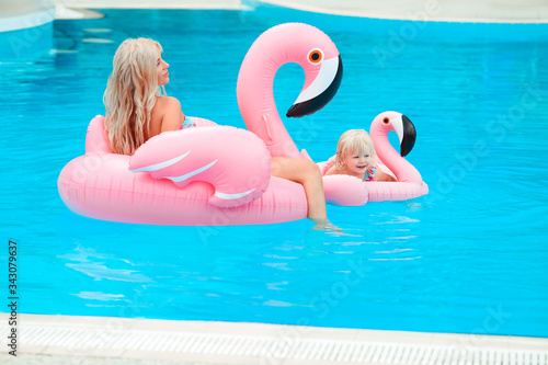 Happy family look summer vacations. Beautiful mother having fun with daughter.  Blonde pretty woman with her little girl wears in fashion same swimwears relax on pink Inflatable pool float flamingo. © Victoria Andreas