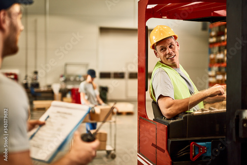 Happy forklift operator talking with a foreman while working in a warehouse.