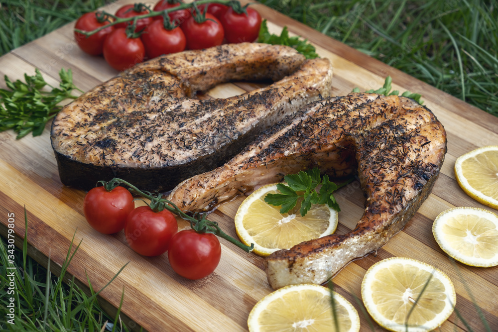 Baked salmon fish steak with tomatoes, herbs, lemon slice and spices. Smoked trout on green grass. Grilled seafood with vegetables on wooden table. Diet menu Baked salmon fish steak with tomatoes, herbs, lemon slice and spices. Smoked trout on green grass. Grilled seafood with vegetables on wooden table. Diet menu