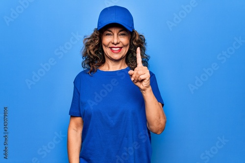 Middle age beautiful delivery woman wearing blue uniform and cap over isolated background smiling with an idea or question pointing finger up with happy face, number one