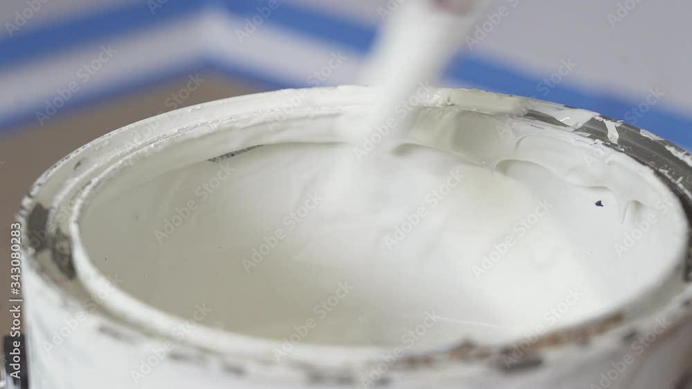Hand of painter dipping a brush into a bucket with white paint. The paint drips from the brush into the bucket Hand of painter dipping a brush into a bucket with white paint. The paint drips from the brush into the bucket