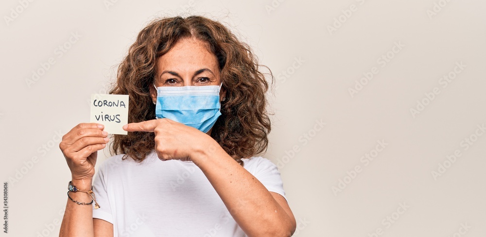 Middle age woman wearing coronavirus protection mask holding virus disease reminder paper smiling happy pointing with hand and finger Middle age woman wearing coronavirus protection mask holding virus disease reminder paper smiling happy pointing with hand and finger