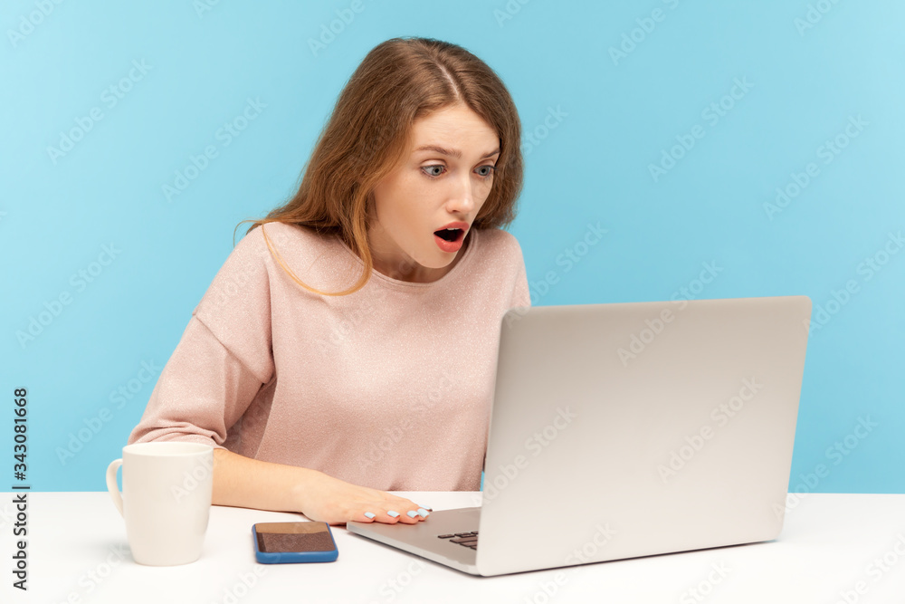 Wow, unbelievable! Young woman with shocked expression looking at laptop screen with open mouth, talking on video call, online conference from home office. indoor studio shot isolated, blue background Wow, unbelievable! Young woman with shocked expression looking at laptop screen with open mouth, talking on video call, online conference from home office. indoor studio shot isolated, blue background