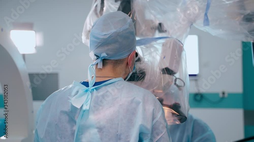 Doctors perform a neurosurgery. Two neurosurgeons looking into contemporary microscope during microsurgery in the operating theatre.