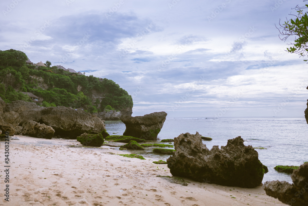 Beautiful deserted beach on the island of Bali at sunset. Rocks and nature. Plants and houses on the coast. Tropical paradise. Stones and white sand on the ocean